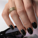 Vernis semi-permanent professionnel CND Shellac Opulent Onyx noir profond pailleté doré appliqué sur ongles avec effet scintillant